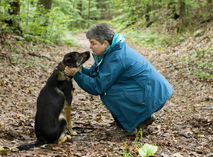 Asha, a border collie mix, leans in as Marilyn Webster kneels to praise her during their walk.